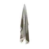 Lucienne Throw in green, woven fabric draping with fringed edges, fading from solid green to light grey with a flecked grass-like pattern, shown against a plain white background.