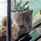 Sayah Stoneware Plant Pot in grey with dimpled texture and narrow foot, holding a succulent on a dark shelf with decorative stones nearby.