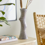 Raheem Stoneware Vase 34cm in grey, with a twisted, textured ceramic body holding dried stems, shown on a sideboard in a living room setting.