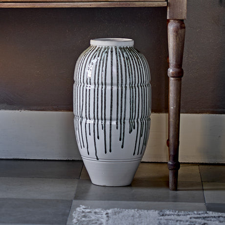 Scarlet Stoneware Vase 47cm in white with dark drip-glaze stripes and ridged texture, standing on a tiled floor beside a wooden table leg.