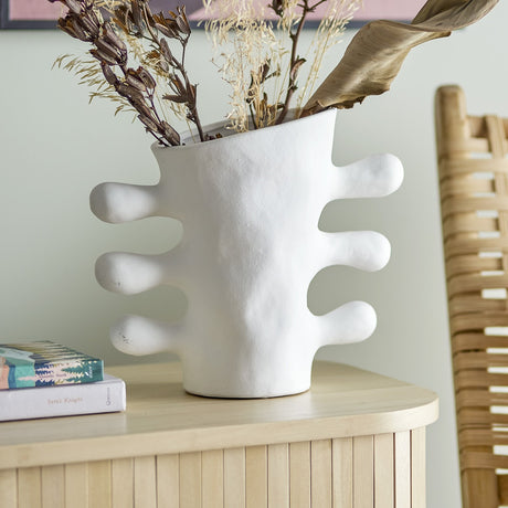 Pernilla Stoneware Vase 26cm in white with sculptural branch-like arms, holding dried foliage on a wooden sideboard beside books and a woven chair.