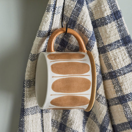 Linora Stoneware Mug from the set of 3, white glaze hand-painted with tall ovals and fine lines, wooden handle, shown hanging from a checked kitchen towel.