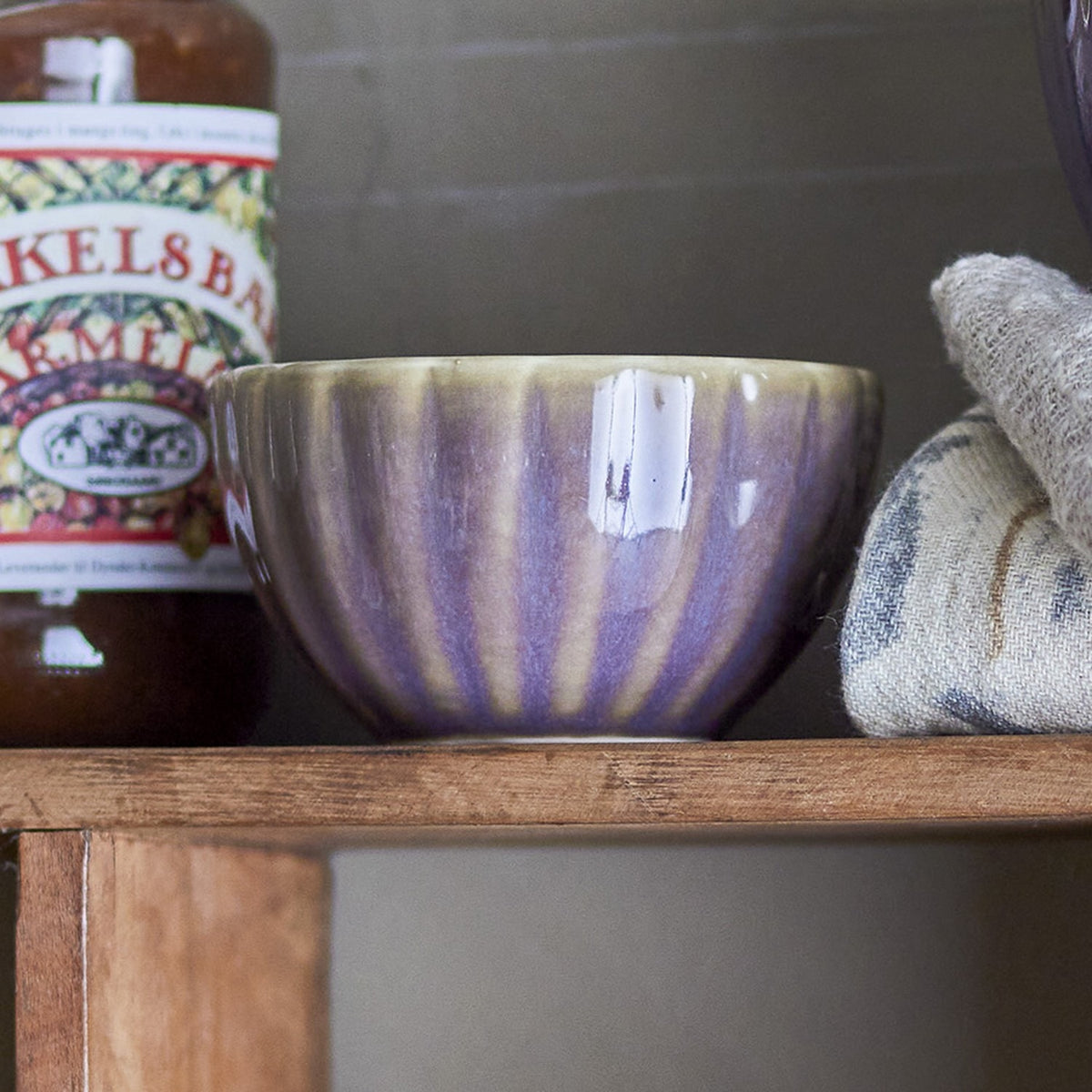 Latina Stoneware Bowl 9cm in grey with vertical ribbed fluting, shown on a wooden shelf beside a jar and folded cloths.
