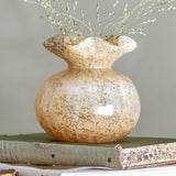 Thebe Glass Vase 12cm in Amber, a round-bodied glass vase with a pinched neck and ruffled rim, speckled finish, shown with dried grasses on a stack of books.