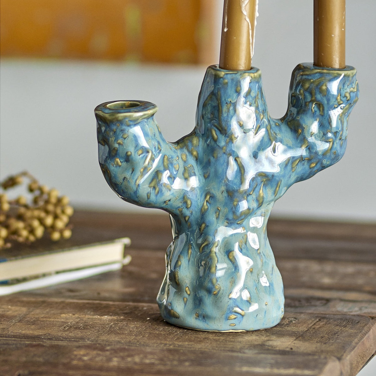 Tahoka Stoneware Candle Holder in blue ceramic with a tree-like branching form and three uneven arms, holding lit taper candles on a wooden table.