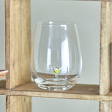 Misa Floral Tumbler in clear mouthblown glass with a stemless, rounded body and a small flower detail rising from the base, displayed on a wooden shelf.