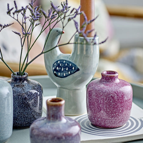Trudy Bird Stoneware Candle Holder in green, shaped like a perched bird with a painted wing of teardrop dots, holding a taper candle, displayed among small ceramic bud vases with dried flowers.