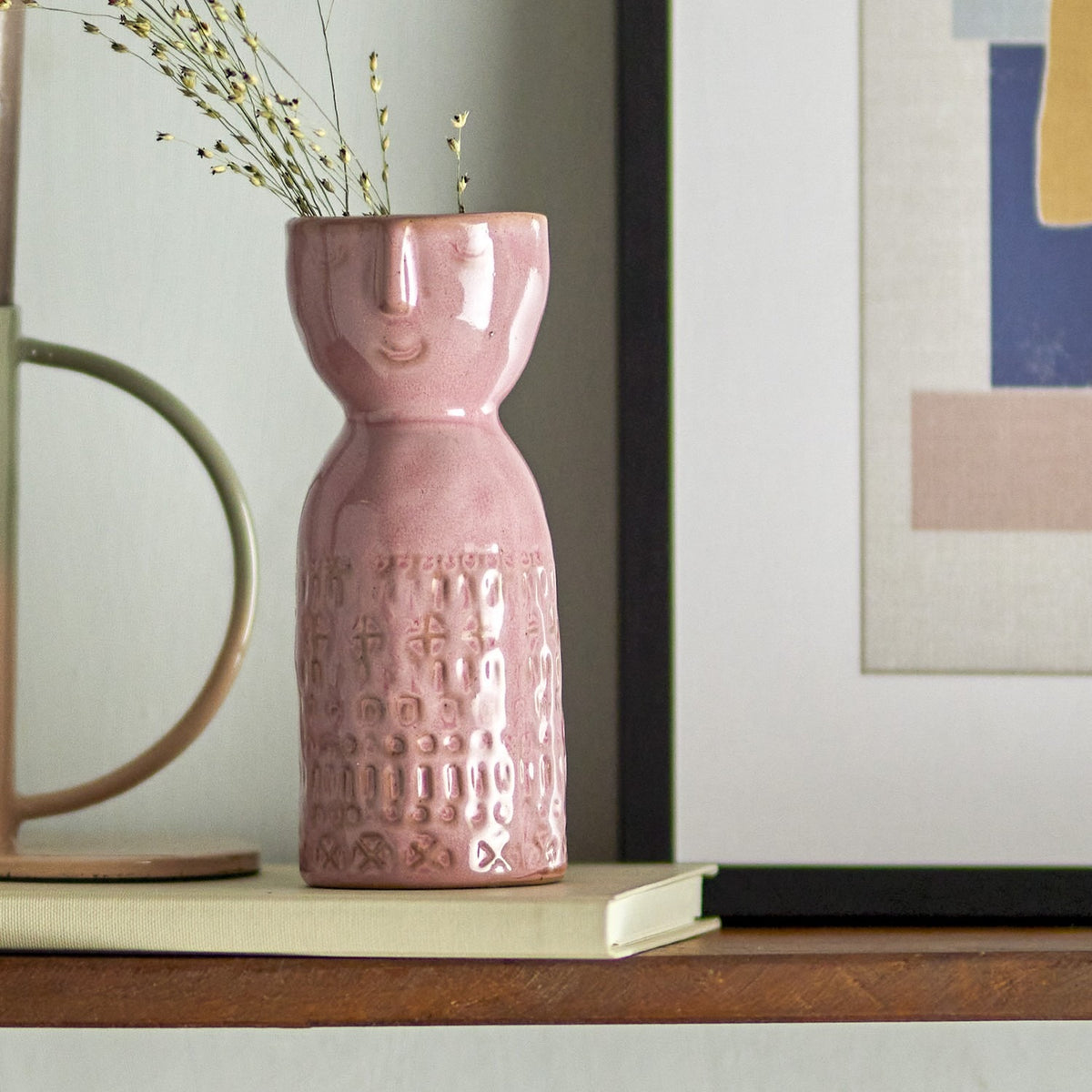 Pink stoneware vase, Embla 14.5cm, with a sculpted face at the neck and embossed geometric pattern below, shown on a shelf with dried flowers.