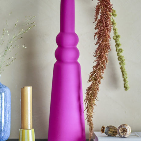 Isolde Stoneware Vase 28.5cm in pink with a matt finish, slim tapering body and ribbed neck, styled with dried foliage and candles against a neutral wall.
