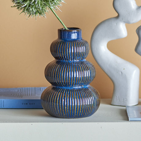 Myrtle Striped Stoneware Vase 20cm in blue, three ribbed rounded tiers with a short neck, shown on a shelf beside books and a grey sculptural ornament.