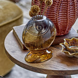 Varga Fish Glass Vase 16cm in amber, fish-shaped with flared foot and raised eye detail, styled on a wooden table with dried flowers and decorative accents.