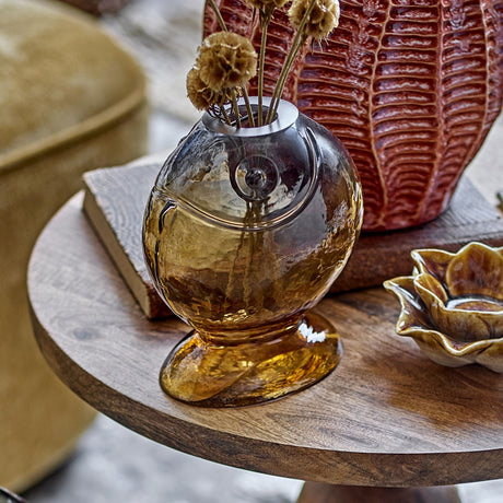 Varga Fish Glass Vase 16cm in amber, fish-shaped with flared foot and raised eye detail, styled on a wooden table with dried flowers and decorative accents.