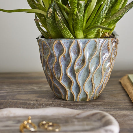 Feren Stoneware Plant Pot in blue, a small ceramic planter with wavy raised texture and speckled glaze, shown holding a green plant on a wooden surface.