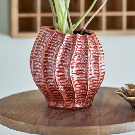 Callon Stoneware Vase 20.5cm in pink with ribbed, seashell-like ridges and a scalloped rim, holding greenery on a wooden table.