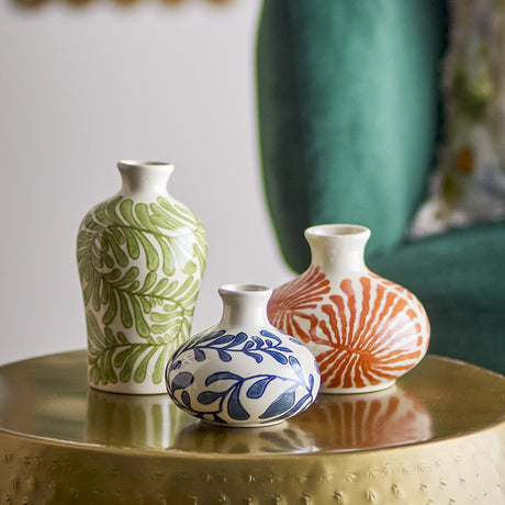Fauni Leaf Stoneware Vases Set of 3 in white with hand-painted green, blue, and orange leaf patterns, shown on a gold tray table with a teal chair in the background.