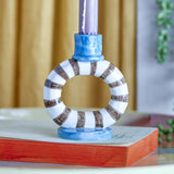 Tacana stoneware candle holder with an open striped ring in white and brown, blue cup holding a lilac taper candle, set on an oval base.
