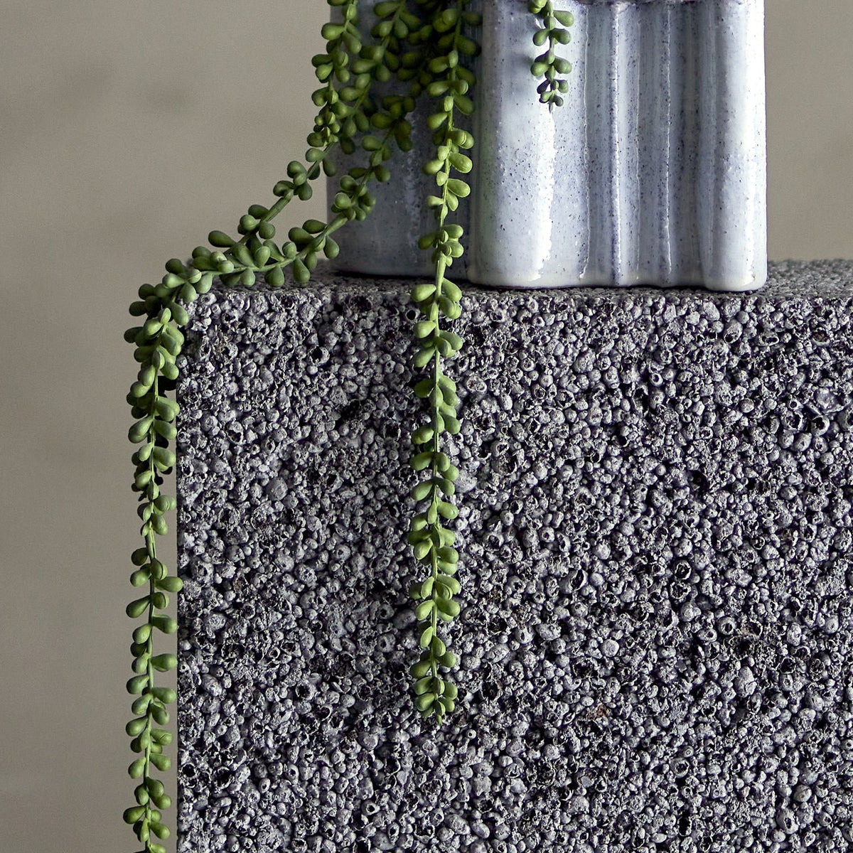 Pearl Artificial Plant - Green, trailing faux foliage with beaded round leaves on fine stems, draped over a textured grey concrete plinth beside a ribbed stoneware vase.