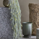Willow Artificial Plant in green cascading with fine, needle-like trailing foliage from a textured grey vase, styled beside stone decor and a green ceramic pot.