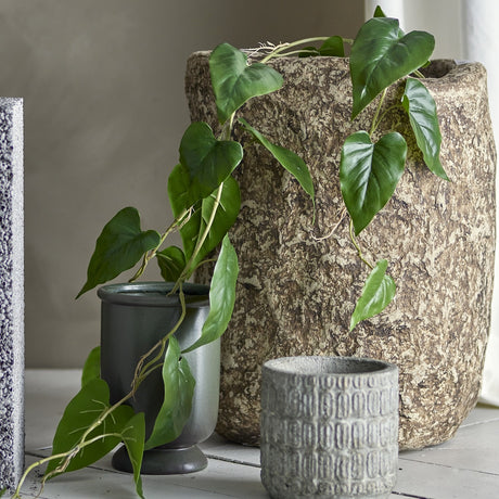 Anthurium Artificial Plant in green, a trailing stem of heart-shaped leaves spilling from a textured stone-effect pot, styled beside smaller ceramic planters.