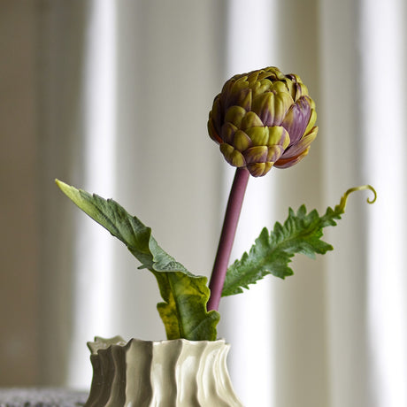 Protea Artificial Stem 54cm in purple, showing a layered bract flower head on a purple stem with two deeply cut leaves, displayed in a ridged cream vase against a curtained background.