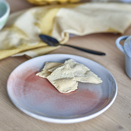 Stoneware side plate from the Paula Breakfast Set in orange reactive glaze, shown with crackers on a wooden table beside a spoon and linen napkin.