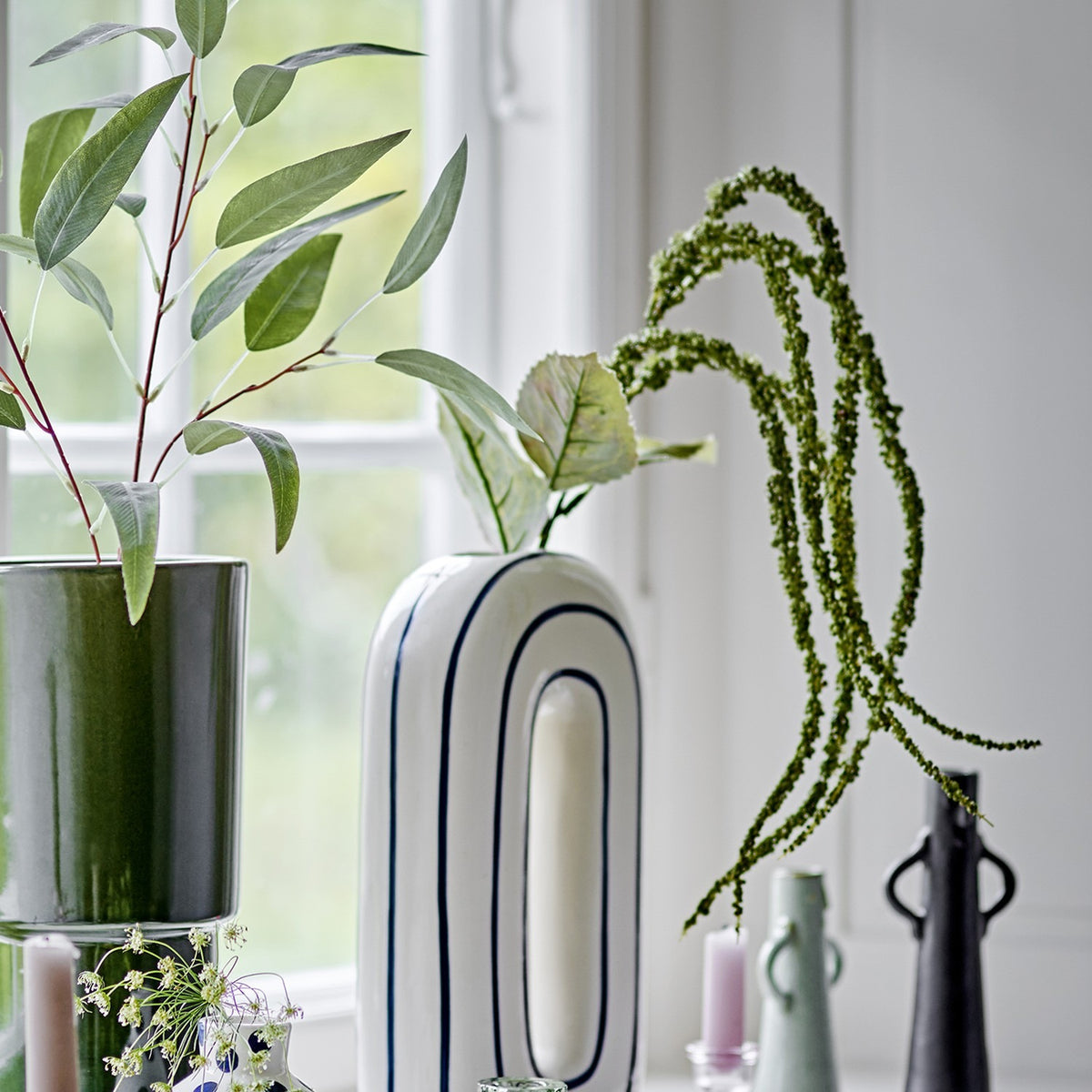 Foxtail Artificial Stem in green, trailing beaded tassels and broad leaves arching above ceramic vases on a windowsill.