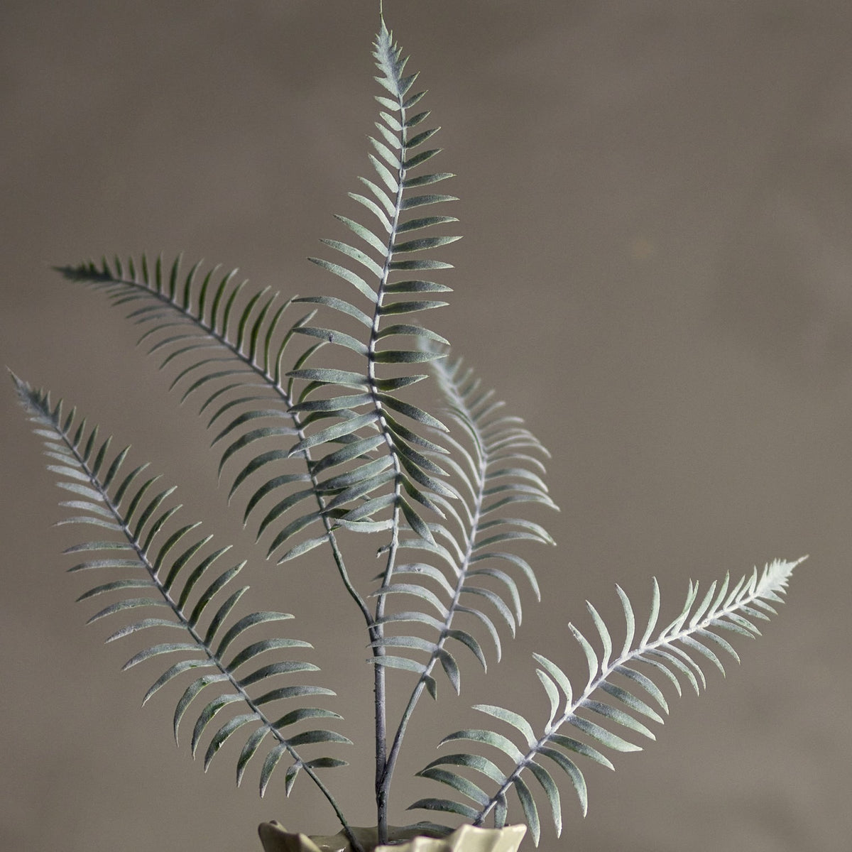 Sago Artificial Stem in green, a faux fern-like branch with arching fronds of narrow leaflets, shown upright in a vase against a plain brown background.
