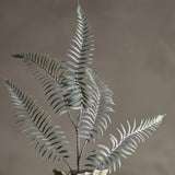 Sago Artificial Stem in green, a faux fern-like branch with arching fronds of narrow leaflets, shown upright in a vase against a plain brown background.