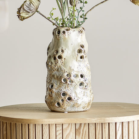 Noble Stoneware Vase 21.5cm in beige with a pitted, coral-like textured glaze, holding dried stems, set on a wooden table against a neutral background.