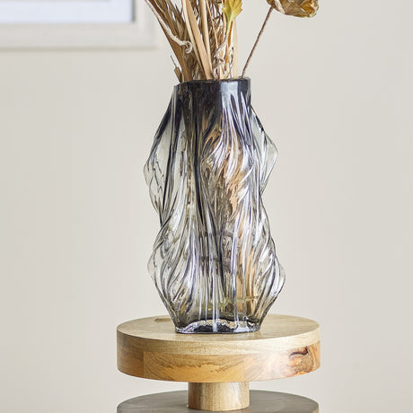 Tulla Wavy Glass Vase 32cm in Grey, mouth-blown rippled glass with an uneven rim, holding dried stems on a round wooden stand against a neutral wall.