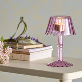 Cisco Glass Tealight Holder 18cm in pink, lamp-shaped with fluted shade and ribbed stem on a fluted foot, lit and displayed on a table beside books and flowers.