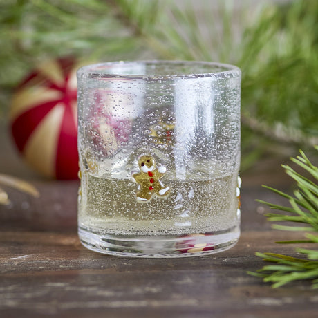 Debra Gingerbread Christmas Tumbler in clear mouthblown glass with bubbled texture and a hand-painted gingerbread figure, shown with sparkling water and festive greenery in the background.