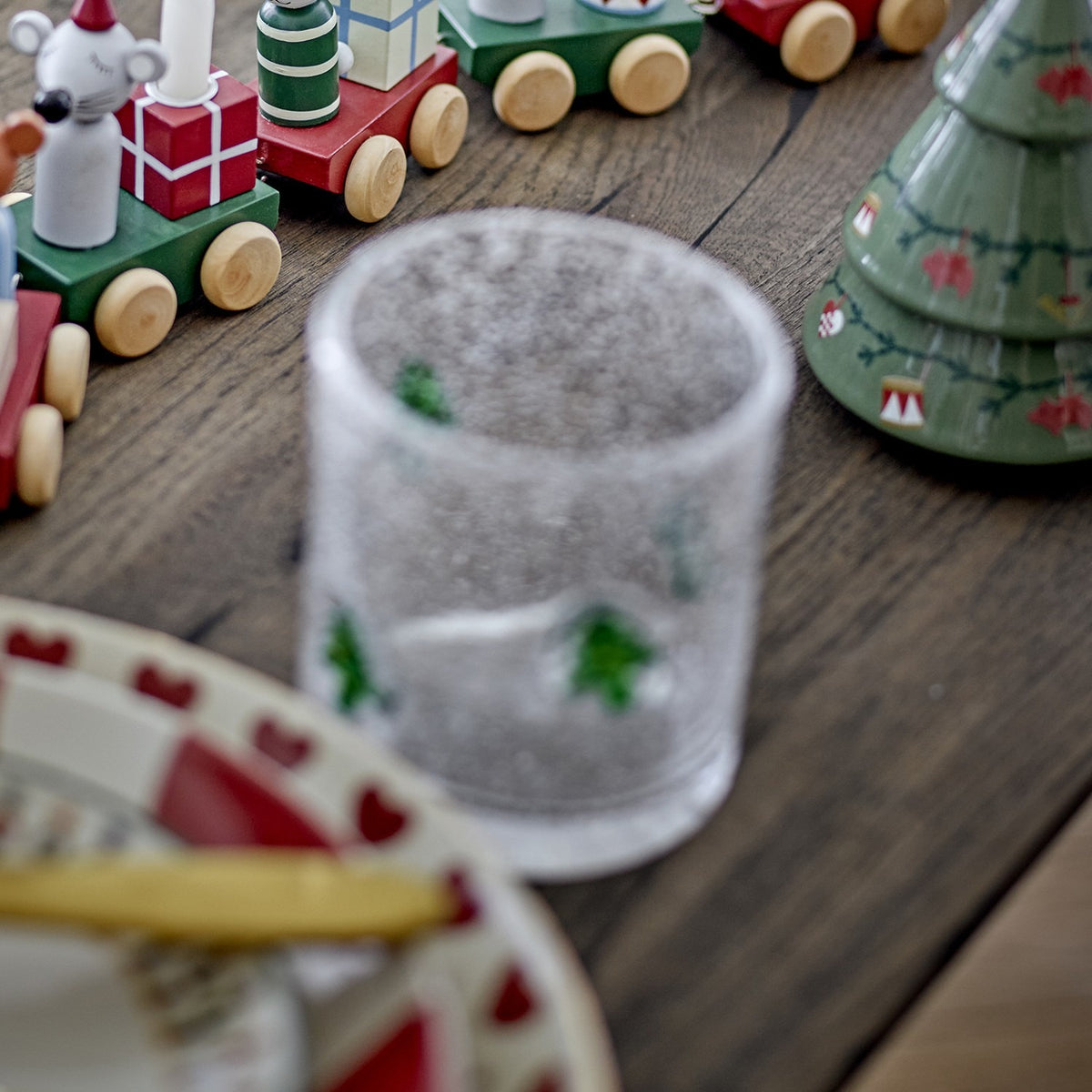 Debra Christmas Tree Tumbler in clear bubbled glass with hand-applied green tree motifs, shown on a wooden table beside festive décor.