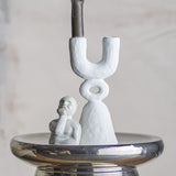 Syra Resin Candle Holder 22cm in White, a two-armed U-shaped design with an open ring link above a flared base, shown with a small figurine on a mirrored tray.