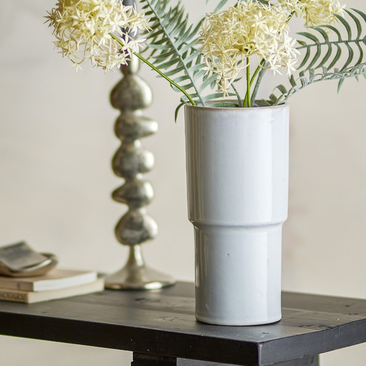 Marji Speckled Stoneware Vase 24cm in white with a stepped, two-tiered cylindrical shape, shown holding greenery and white flowers on a dark wood table.