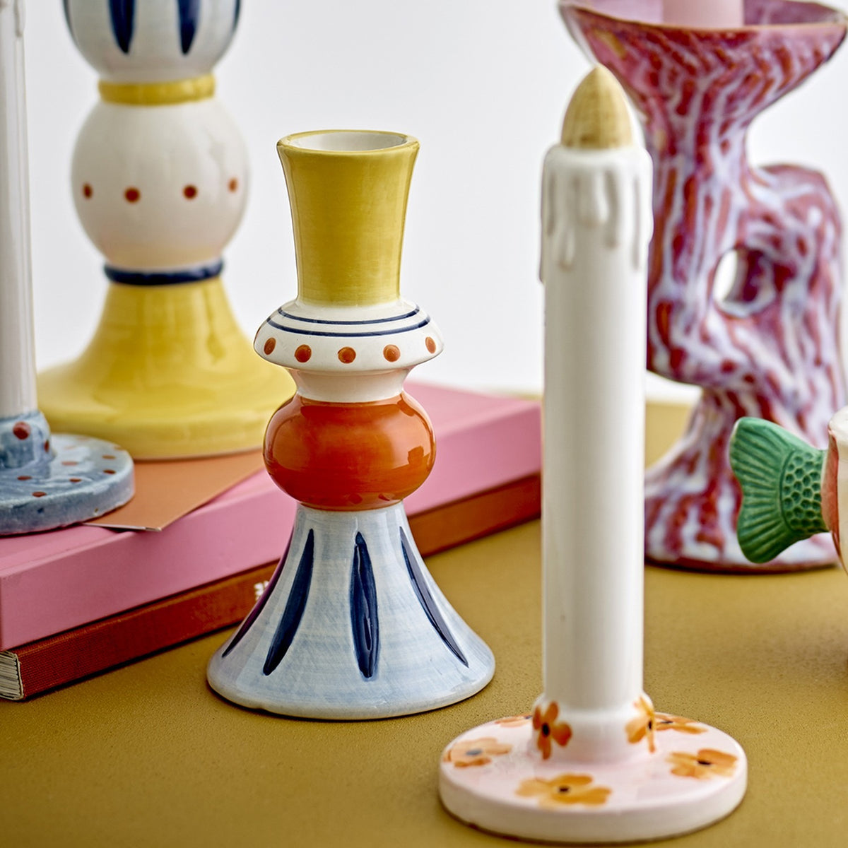 Kairi Stoneware Vase 14cm in Multi, a stacked ceramic bud vase with yellow flared neck, dotted collar, orange rounded middle and blue flared foot with painted stripes, shown among candle holders.