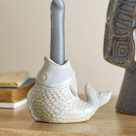 Hiro Fish Stoneware Candle Holder in grey, a fish-shaped ceramic piece with raised scales and curled tail, holding a grey candle on a wooden surface.