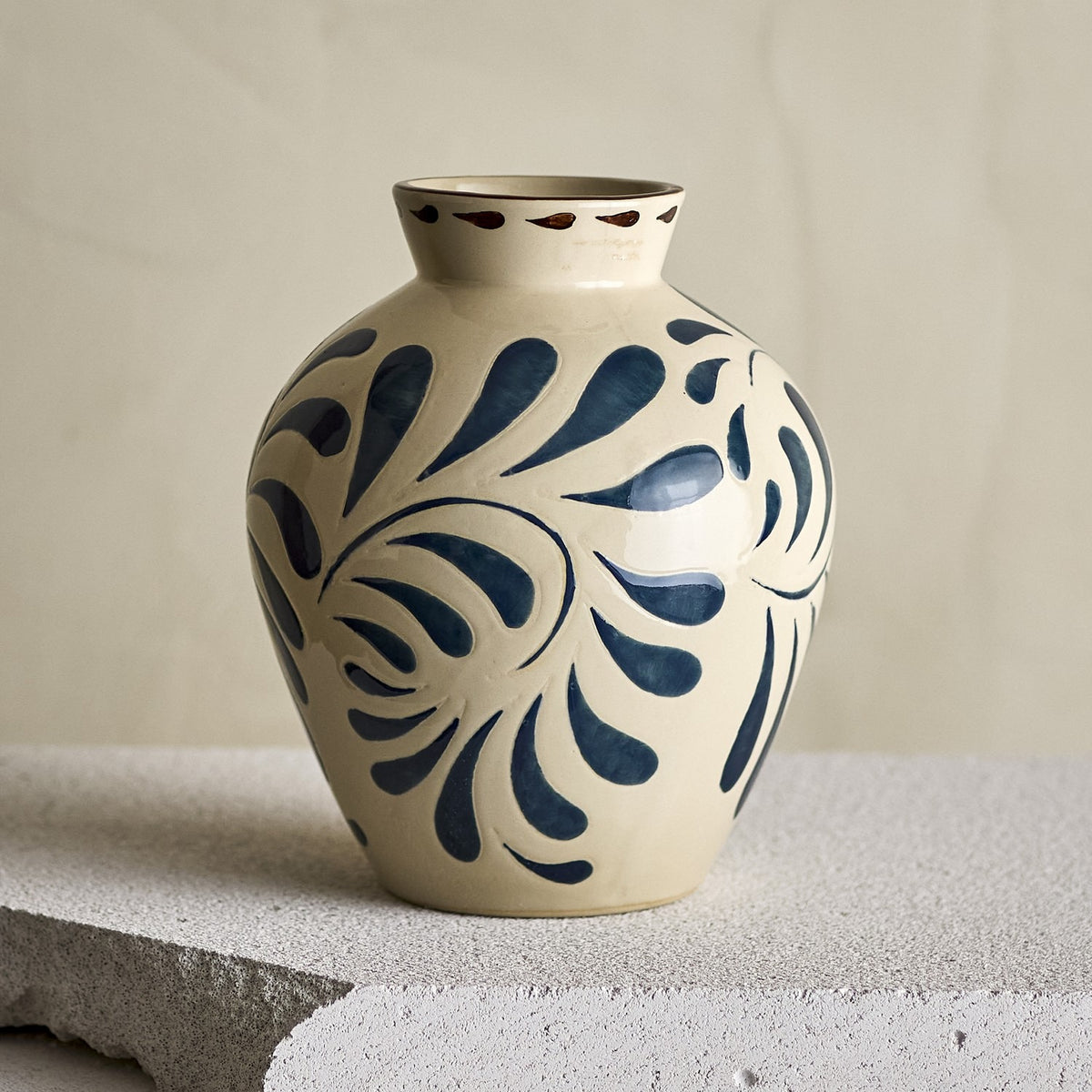 Heikki Stoneware Vase 24cm in cream, rounded ceramic body with bold blue leaf motifs and brown-dashed rim, shown on a stone ledge against a neutral background.