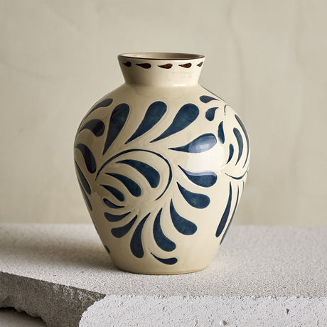 Heikki Stoneware Vase 24cm in cream, rounded ceramic body with bold blue leaf motifs and brown-dashed rim, shown on a stone ledge against a neutral background.