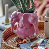 Pontus Stoneware Vase 15.5cm in Pink, shaped as joined elephant heads with trunks and ears, holding a cactus plant on a woven tray in a living room setting.