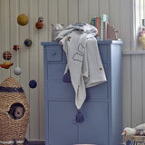 Space Cotton Throw in cream draped over a blue chest of drawers in a nursery, showing a printed rocket, stars and tasselled corners.