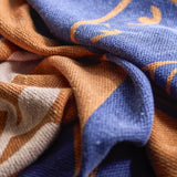 Close-up of the Atle Leaf Cotton Throw in brown, showing woven cotton fabric with a leaf motif in rust, blue, and cream tones.