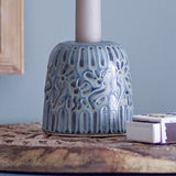 Samsin Floral Stoneware Candle Holder in blue glaze with embossed floral and panel relief, holding a taper candle on a wooden table beside a matchbox.