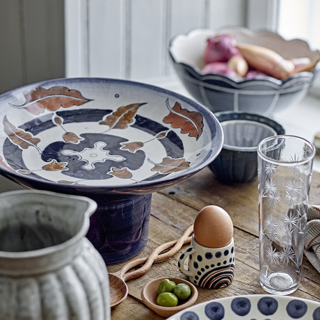 Myrna Stoneware Pedestal Bowl 29cm in Multi, a stoneware pedestal bowl with hand-painted leaf motifs and a star centre on a raised footed base, shown styled on a wooden table.
