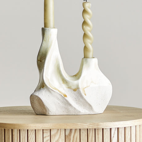 Wavy Speckled Stoneware Candle Holder in cream with two uneven openings holding taper candles, glossy top and sandy-textured base, shown on a wooden table.