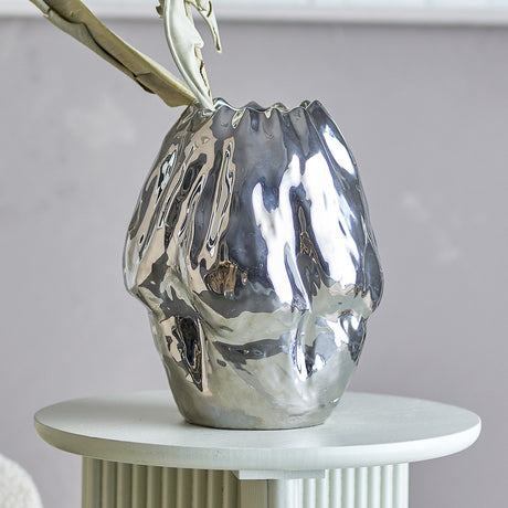 Bobby Stoneware Vase 29cm in Silver, a crumpled-texture ceramic vase with high-gloss finish and wavy rim, shown on a round side table against a grey wall.