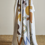 Memmo Cotton Throw in Multi, draped in folds showing bold multicoloured alphabet letters with animal-print detailing on a textured white cotton ground.