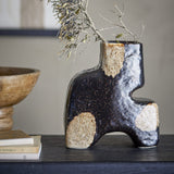 Ollia Stoneware Vase 20cm in Black, glossy rippled finish with rough tan patches and notched silhouette, styled with dried branches on a dark console beside books and a wooden bowl.