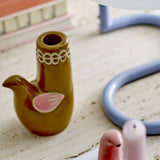 Trudy Bird Stoneware Candle Holder in glossy brown, with bird-shaped body, painted pink wing, and looped rim detail, shown on a light tabletop beside books.