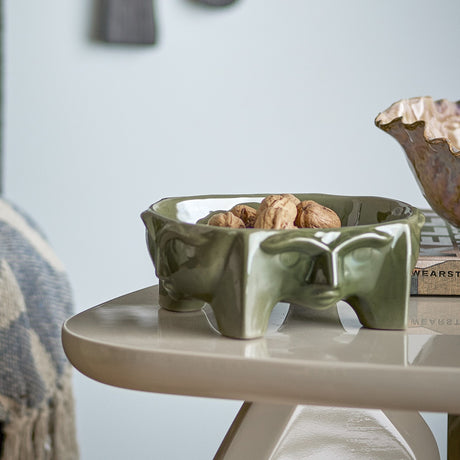 Amilia Stoneware Bowl in green, 21x17.5cm, with a moulded face design and short feet, shown holding walnuts on a side table.